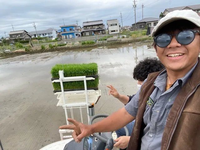 田植えの日、苗を積んだ田植え機の上で笑う丸恵商会のふたり
