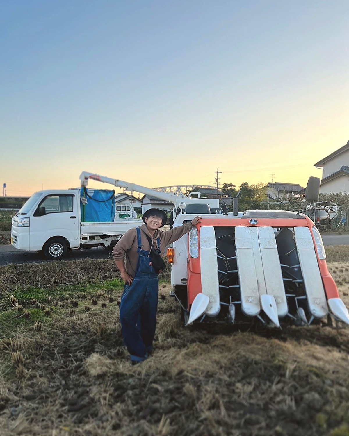 夕暮れの田んぼでコンバインの横に立つ丸恵商会の生産者