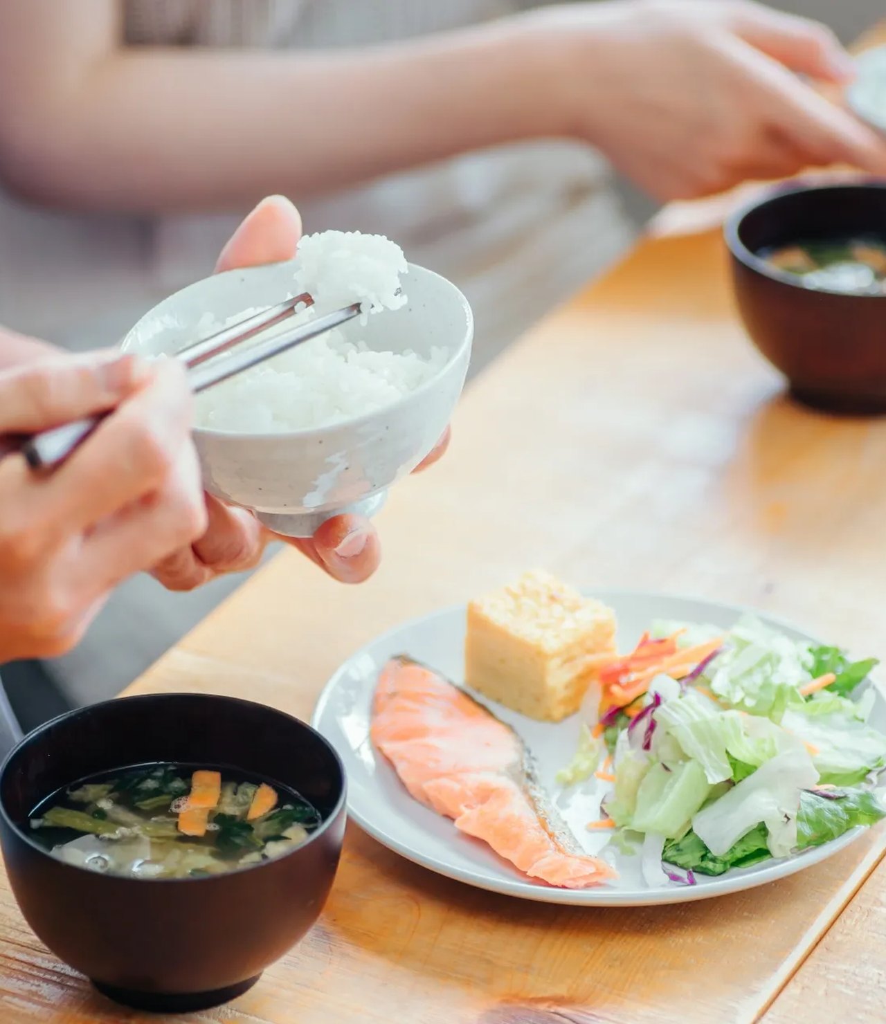 食卓でごはん茶碗によそう手元（米粒のかたちに切り抜いた写真）